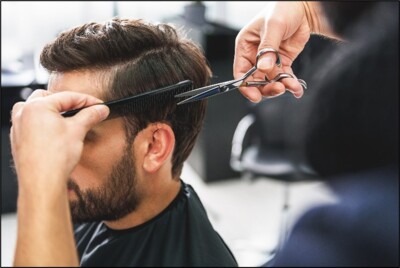 Blick über die Schulter eines Friseurs, der einem Kunden die Haare schneidet.