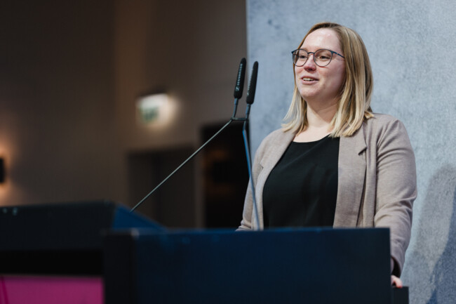 Jessica Ozimec steht am Redepult auf der Bühne und spricht in die Richtmikrofone.