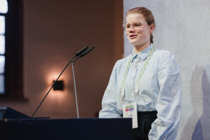 Dorothea Hayh from adesso SE standing at the lectern on stage in front of a gray background.